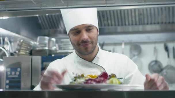 Glad kock i ett kommersiellt kök i en restaurang eller ett hotell serverar sallad. — Stockvideo