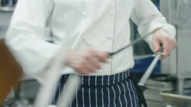 Επαγγελματίας σεφ σε μια εμπορική κουζίνα σε ένα εστιατόριο ή ξενοδοχείο είναι το ακόνισμα μαχαίρια. — Αρχείο Βίντεο