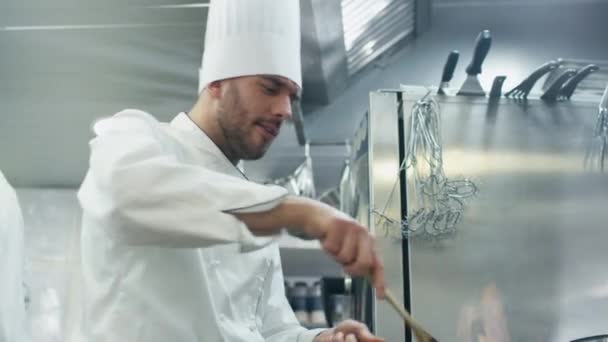 Professional chef in a commercial kitchen is preparing food in flambe style on a pan. — Stock Video