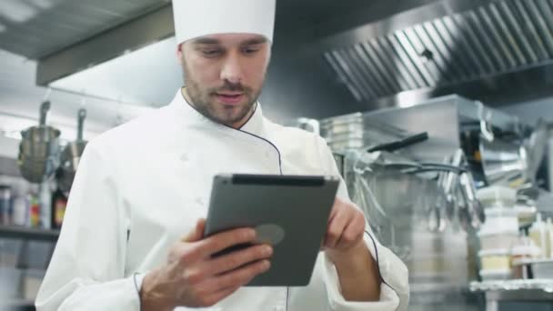 Chef profesional en una cocina comercial en un restaurante u hotel está utilizando una tableta . — Vídeo de stock