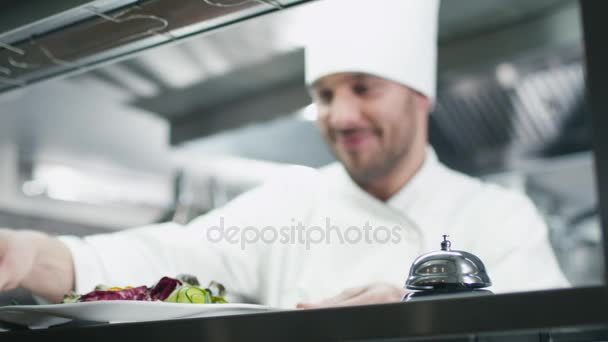 Glad kock i ett kommersiellt kök i en restaurang eller ett hotell serverar sallad. — Stockvideo