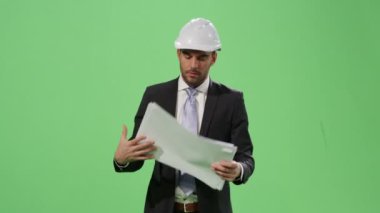İşadamı bir kask ve bir takım elbise içinde yürüyüş ve kağıt belgeleri bir mock-up üzerinde seyir içinde belgili tanımlık geçmiş yeşil ekran.