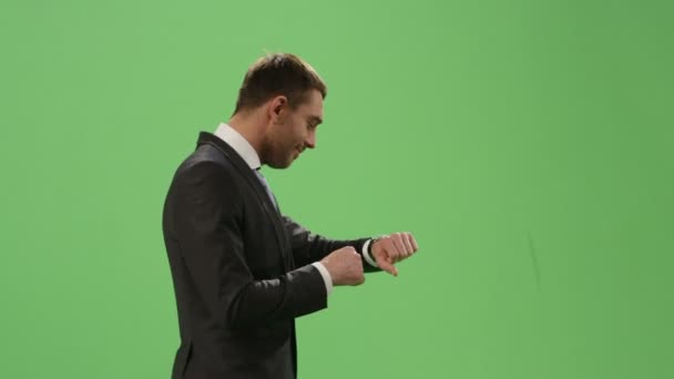 Businessman in a suit is using a smartwatch while walking on a mock-up green screen in the background. — Stock Video