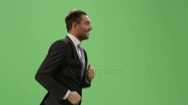Empresário feliz em um terno está correndo em uma tela verde mock-up no fundo . — Vídeo de Stock
