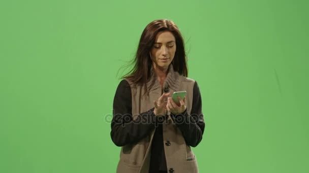 Casual brunette female is walking and using a smartphone on a mock-up green screen in the background. — Stock Video