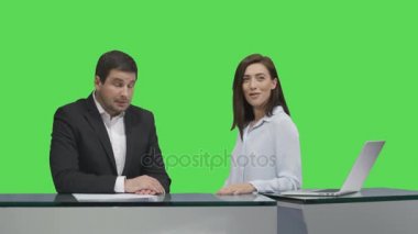 Erkek ve dişi yayıncılar bir masada oturan ve bir mock-up üzerinde konuşurken arka planda yeşil ekran.