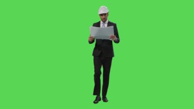 İşadamı bir kask ve bir takım elbise içinde bir mock-up kağıtları ile yürümek içinde belgili tanımlık geçmiş yeşil ekran.