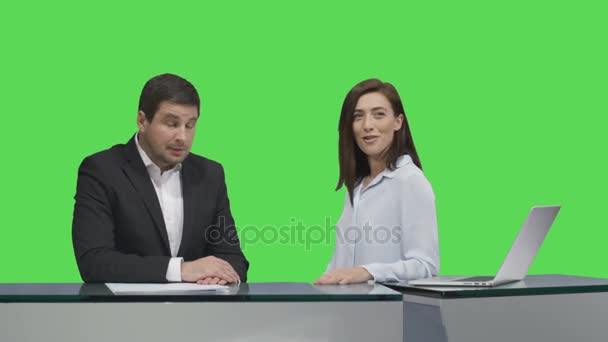 Αρσενικά και θηλυκά ραδιοτηλεοπτικοί φορείς κάθεται σε ένα τραπέζι και να μιλάμε για μια μακέτα πράσινη οθόνη στο παρασκήνιο. — Αρχείο Βίντεο