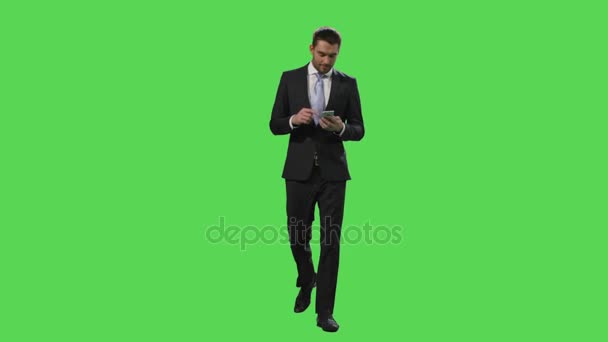 Empresario en un traje está utilizando un teléfono inteligente mientras camina en una pantalla verde simulada en el fondo . — Vídeos de Stock