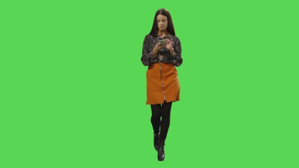 Casual menina morena está andando e usando um smartphone em uma tela verde mock-up no fundo . — Vídeo de Stock