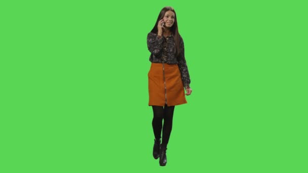 Casual menina morena está andando e falando no telefone em uma tela verde mock-up no fundo . — Vídeo de Stock