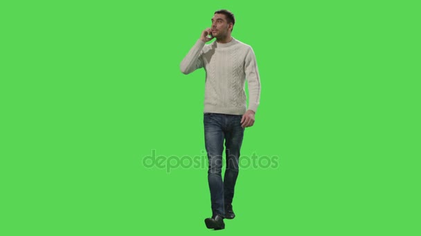 Caucasien occasionnel homme marche et parle au téléphone sur un écran vert maquette en arrière-plan . — Video