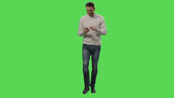 Lässiger kaukasischer Mann geht und benutzt Smartphone auf einem grünen Bildschirm-Attrappe im Hintergrund. — Stockvideo