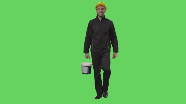 Bouwvakker in een harde hoed bedrijf een emmer met verf loopt op een mock-up groen scherm op de achtergrond. — Stockvideo