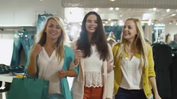 Tres niñas felices están caminando a través de una tienda de ropa en prendas de colores . — Vídeo de stock