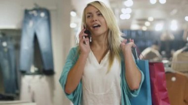 Mutlu genç sarışın kız yine de telefonda konuşurken bir giyim mağazası yürüyor.