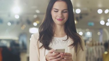 Mutlu genç esmer kız mağaza ve manifatura bir smartphone cep telefonu ile mesaj duruyor.