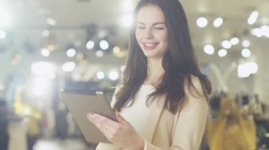 Mutlu genç esmer kız bir mağazada duran ve bir tablet bilgisayar kullanarak.