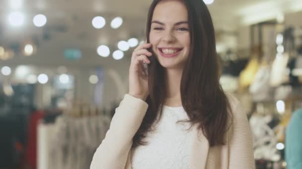 Ευτυχισμένος νεαρή μελαχρινή γυναίκα στέκεται σε ένα πολυκατάστημα και μιλάει στο τηλέφωνο. — Αρχείο Βίντεο