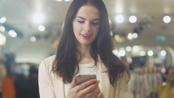 Szczęśliwa młoda brunetka kobieta jest stały w sklepie i przy użyciu smartfonu. — Wideo stockowe