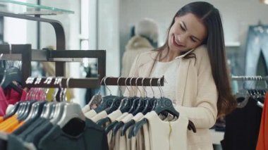 Genç esmer kız elbise süre bir mağaza içinde telefonda konuşmak için alışveriş.