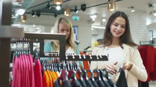 Dos jóvenes felices eligen prendas en una tienda departamental . — Vídeo de stock