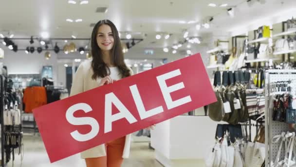Mladá usměvavá brunetka drží znak prodej v obchodním domě. — Stock video