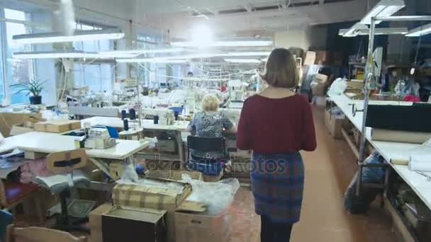 Junge brünette Frau mit Tablette wird beim Gang durch eine Bekleidungsfabrik von hinten erschossen. — Stockvideo