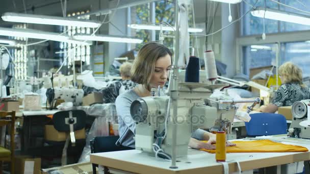 Giovane sarta bruna sta lavorando su una macchina da cucire in una fabbrica di abbigliamento . — Video Stock