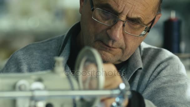 Vecchio in occhiali sta lavorando su una macchina da cucire . — Video Stock