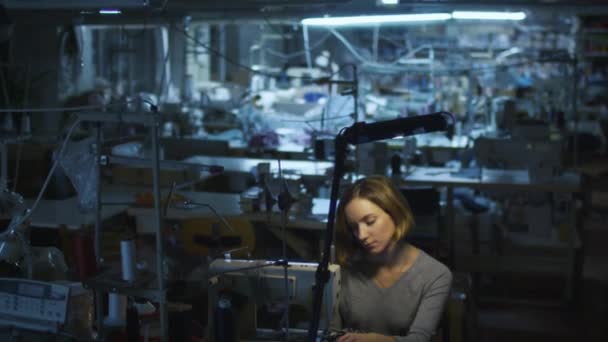 Junge Textilarbeiterin näht während einer Nachtschicht in einer Bekleidungsfabrik, während im Hintergrund das Licht ausgeschaltet wird. — Stockvideo