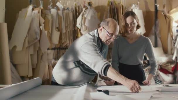 Diseñador de ropa senior sostiene una tableta y muestra el trabajo a una mujer joven . — Vídeos de Stock