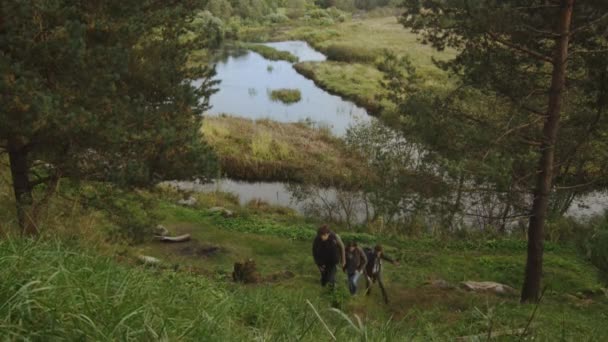 Група чоловіків і жінок піднімаються на пагорб в лісі восени з озером на задньому плані . — стокове відео