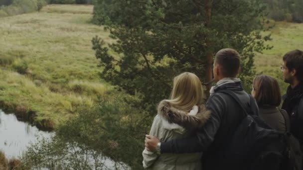 Zwei Paare betrachten von einem Berg aus eine Waldlandschaft mit einem See. — Stockvideo