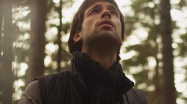 Uzun saçlı adam karanlık sonbahar giysileri ve eşarp bir ormanda ayakta ve etrafa.