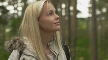 Sarışın kadın beyaz sonbahar paltolu bir ormanda ayakta ve etrafa.