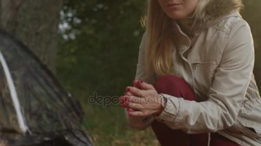 Ellerini bir ormandaki bir kamp ateşi yanında ısınma sarışın bir kadın portresi.