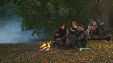 Arkadaş grubu oturup sıcak içecekler ile bir kamp ateşi yanında bir Gölü yakınındaki bir ormandaki bir çadırdan başka bir kız adım iken.
