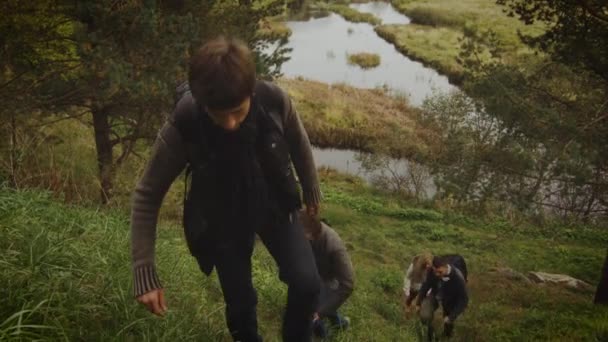 Groep van mannen en vrouwen zijn klimmen een heuvel in een bos in de herfst met een meer op de achtergrond. — Stockvideo