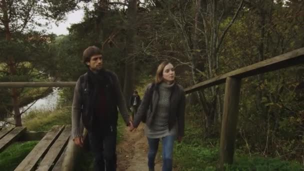 Couple en vêtements d'automne monte sur un sentier forestier avec une rivière en arrière-plan . — Video