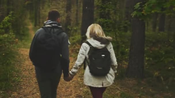 Pareja con mochilas se escapa de la cámara mientras se toma de la mano en un bosque de otoño . — Vídeos de Stock