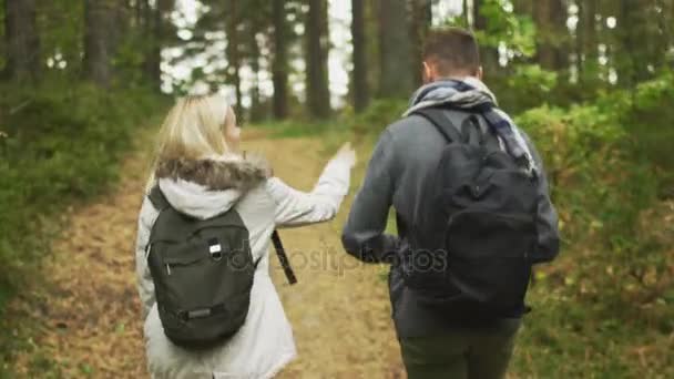 Seguir el disparo desde la parte posterior de una pareja caminando en un bosque de otoño con mochilas . — Vídeo de stock