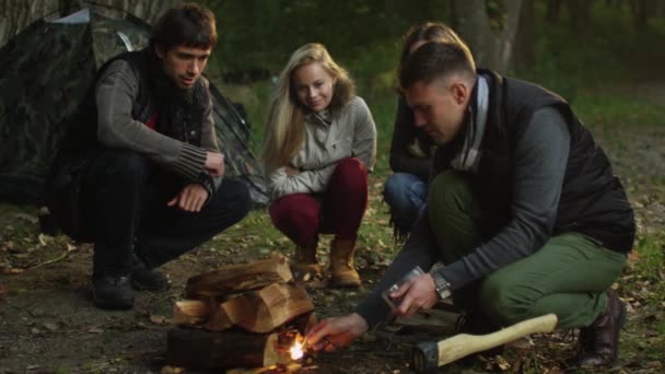 Grupo de personas están sentadas en un bosque y encender una fogata con el fin de calentarse . — Vídeos de Stock