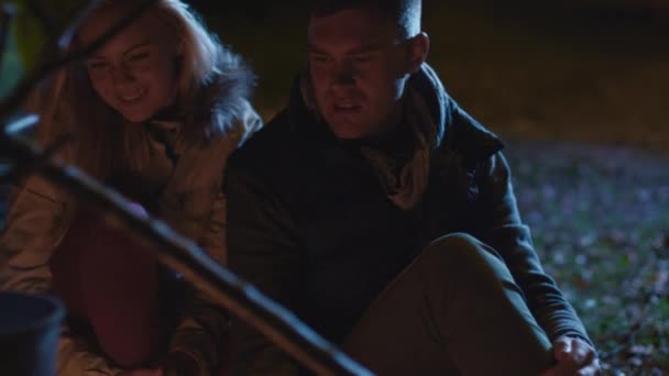 Young couple sit next to a campfire at night and hug each other. — Stock Video