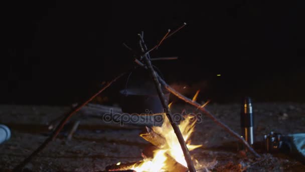 Plan en mouvement d'un feu de camp avec un pot en métal qui brûle la nuit . — Video