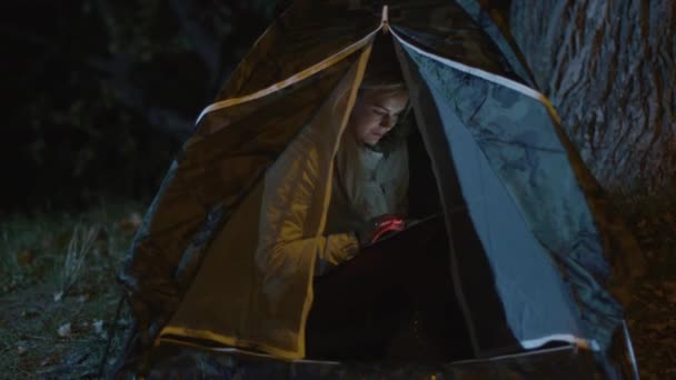 Jovem loira está usando um tablet em uma tenda à noite . — Vídeo de Stock