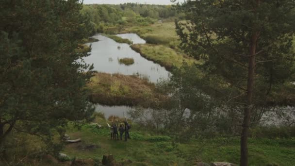 Dos parejas están mirando un paisaje forestal con un lago desde una colina . — Vídeo de stock