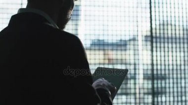 İş takım elbiseli adamı tablet bir çatı katında büyük bir pencere yanında kullanma.