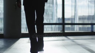İş takım elbiseli adamı güneş ışığı yansıtan binaları görünüyor büyük bir pencere doğru yürüyor.