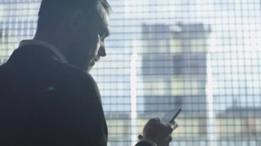 İş takım elbiseli adamı bir garaj büyük bir pencerede yanındaki bir akıllı telefon kullanıyor.